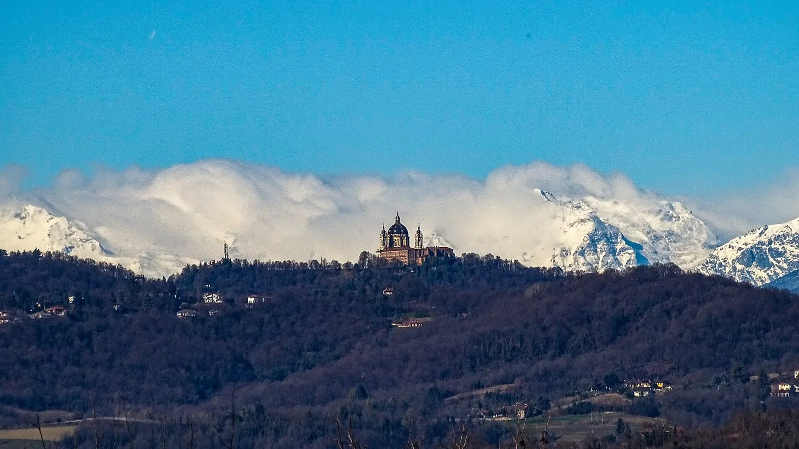 La Basilica di Superga sulla cima della collina boscosa di Torino, con le Alpi innevate e le nuvole sullo sfondo